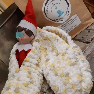 an elf on the shelt elf with an eye covering in a cozy slipper in front of a bag of coffee